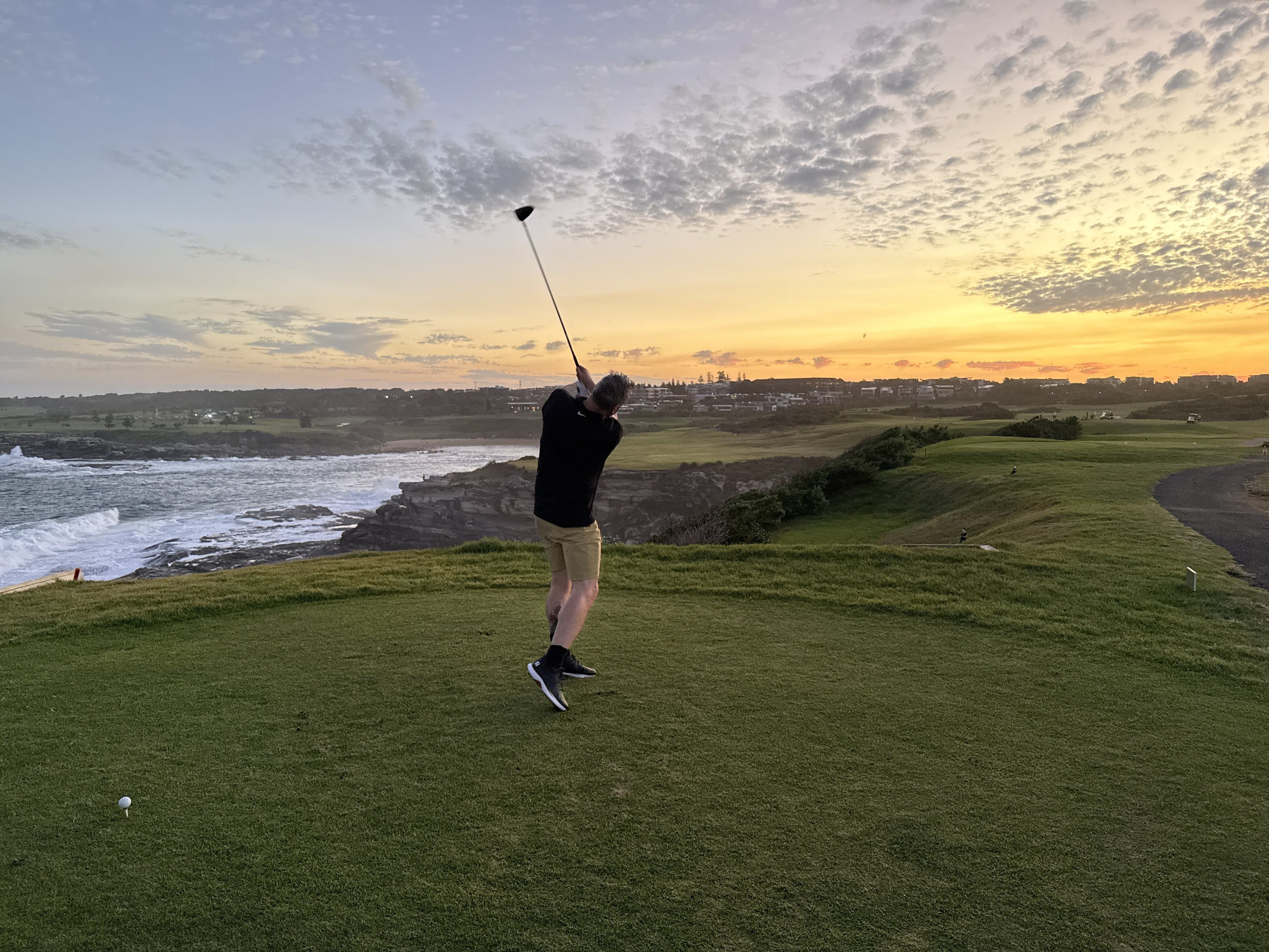 One of the crew holding the finish on a clifftop tee at Little Bay, the sun going down over the surf